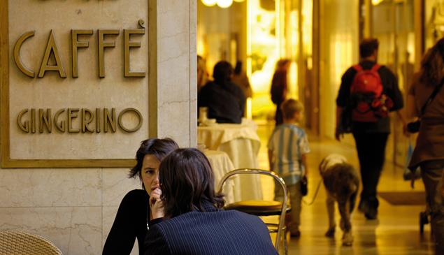 People chatting outside Caffè Gingerino in Bozano, with shoppers walking through the Lauben in the background.