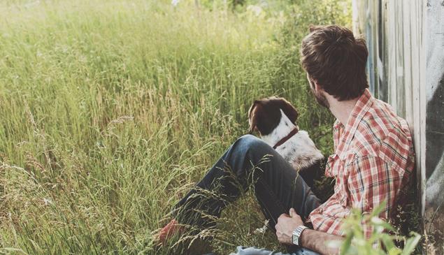 A man and a dog are sitting on grass